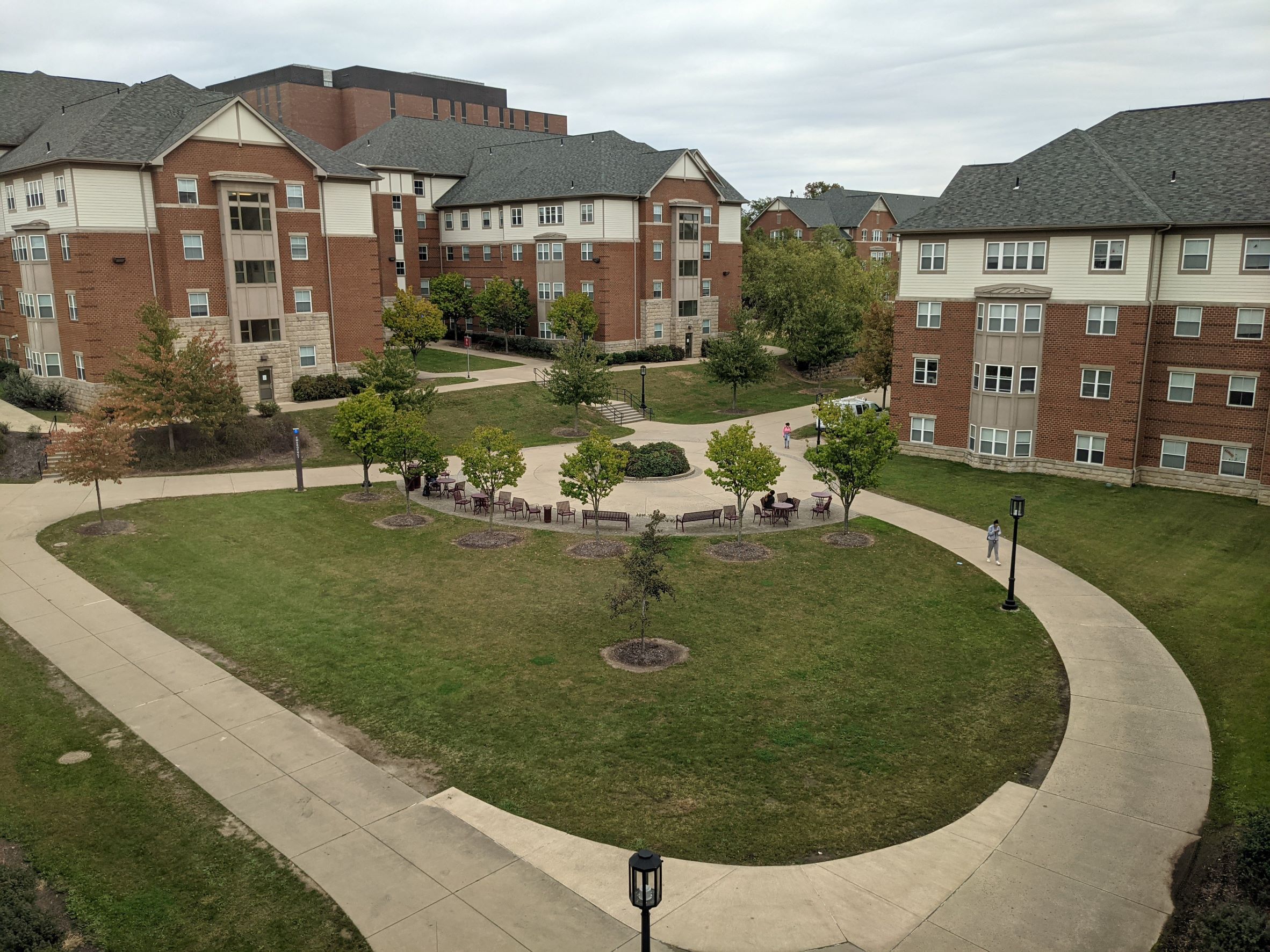 Aerial view of courtyard with swooping sidewalks and central gathering area surrounded by traditional red brick living learning student housing community dormitory buildings