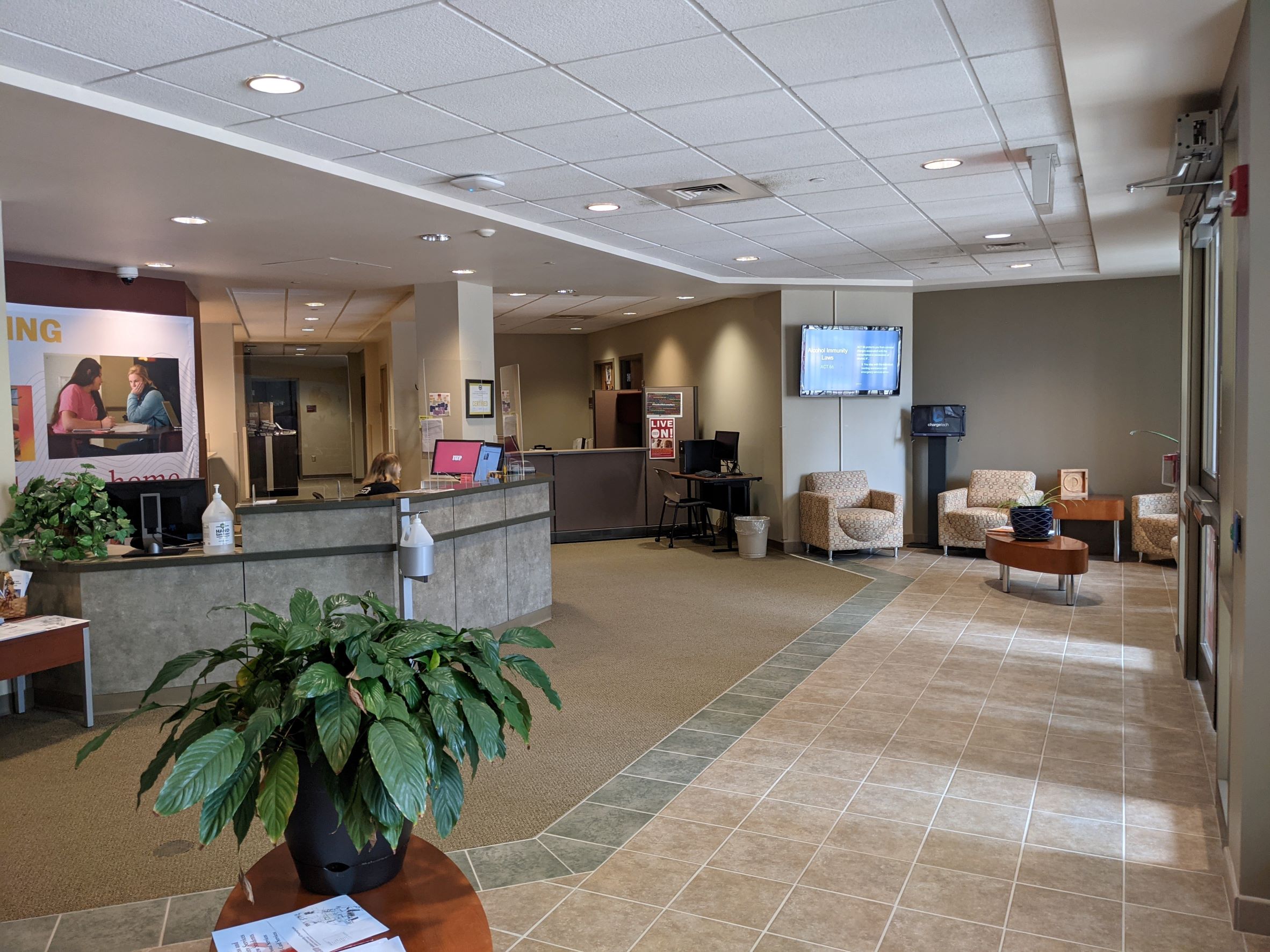 Campus Office of Residence Life offices with contemporary gray reception desk, white ceiling tile, carpet and ceramic tile lobby, olive green walls, furniture and plants