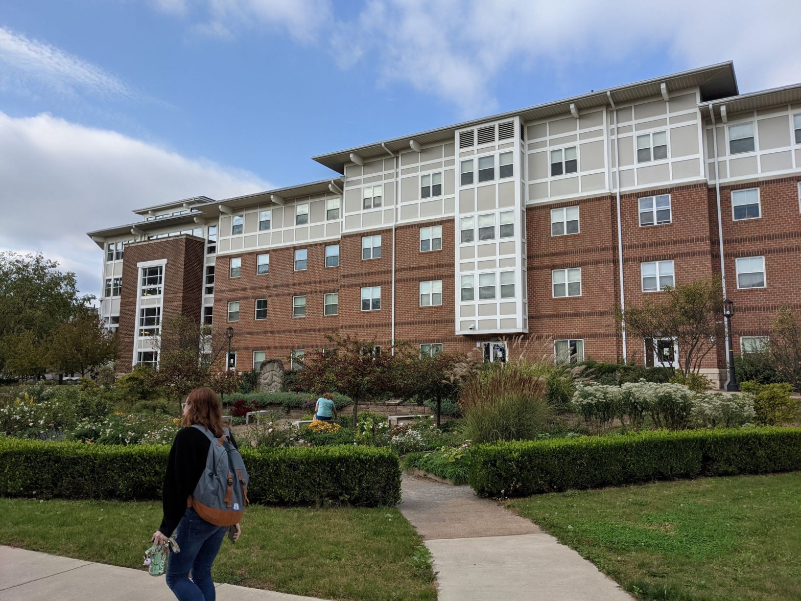 Arts and crafts style living learning student housing community dormitory buildingwith pink brick and white trims with large garden and student walking in foreground