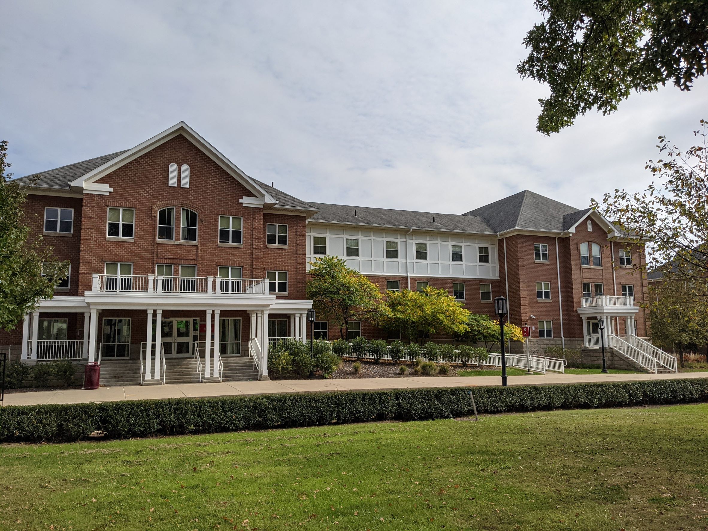 Historical looking pink brick living learning residence hall with many gabled roofs, white front porch and trim, truncated dormer windows and brick quoining, very classical looking building (designed in style of Sutton Hall, the old campus Main)