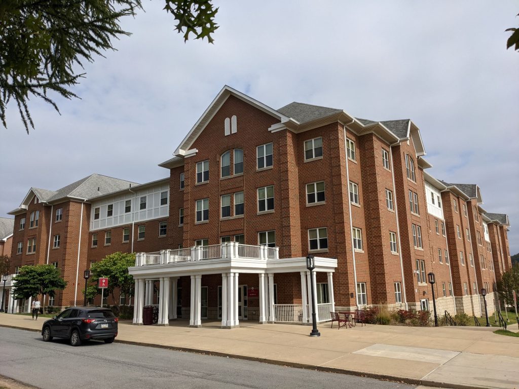 Historical looking pink brick residence hall with many gabled roofs, white front porch and trim, truncated dormer windows and brick quoining, very classical looking building (designed in style of Sutton Hall, the old campus Main) outside of Pittsburgh Pennsylvania