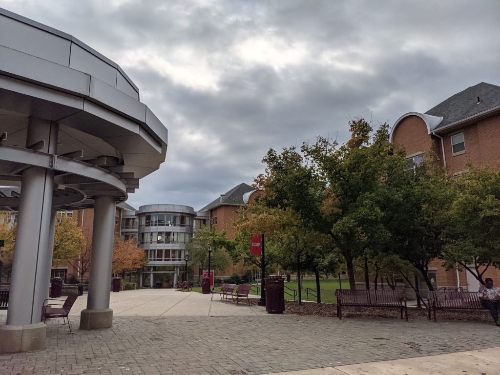 Large UFO looking metal gazebo in front of orange brick contemporary residence hall with cylindrical glass and metal building connecting two buildings in the background outside of Pittsburgh Pennsylvania