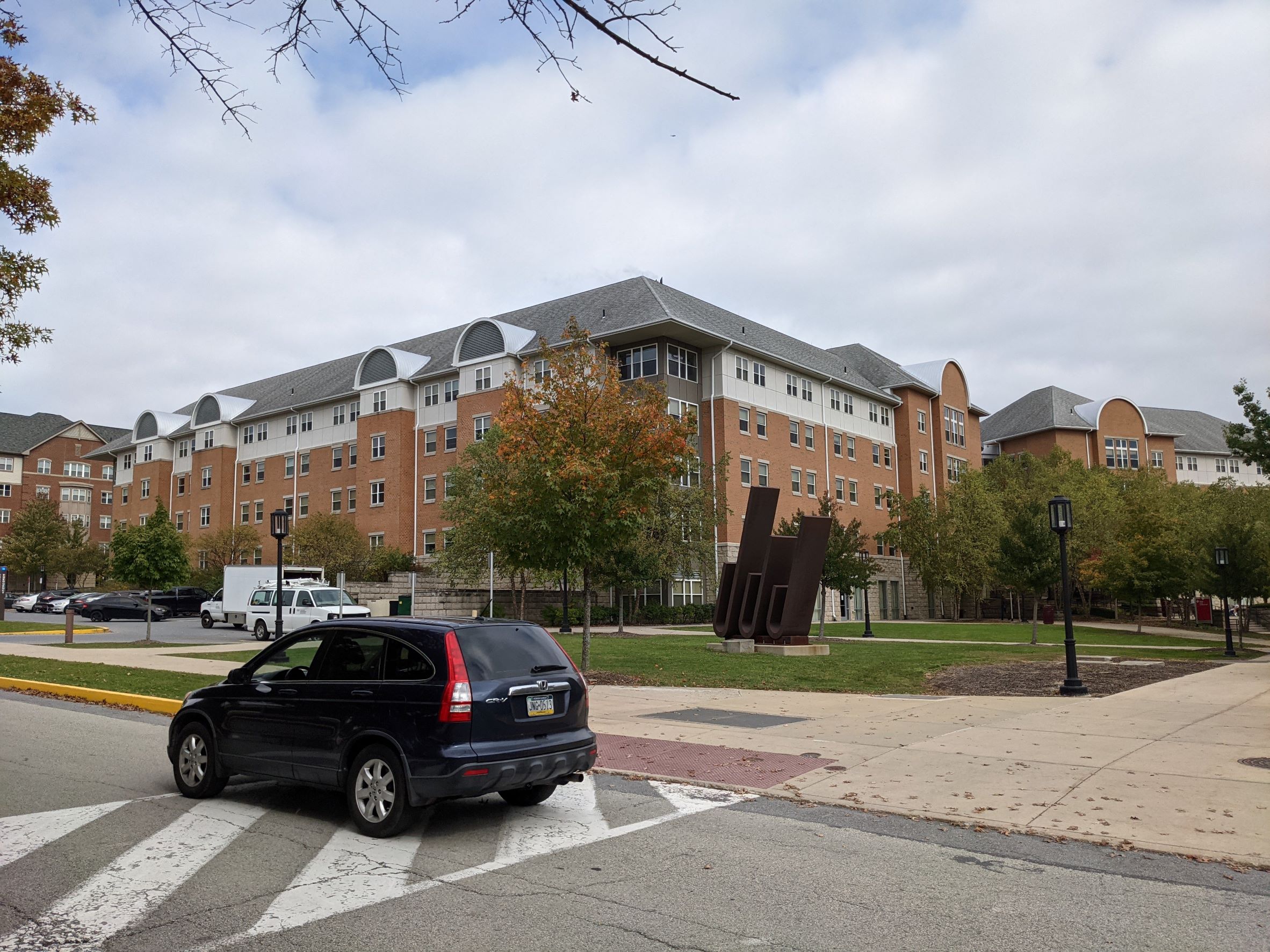 Orange Brick contemporary on-campus living learning student housing community dormitory building with tan clerestory and gray roof, silver barrel vaults at gables, and dark gray corner with glass recessed