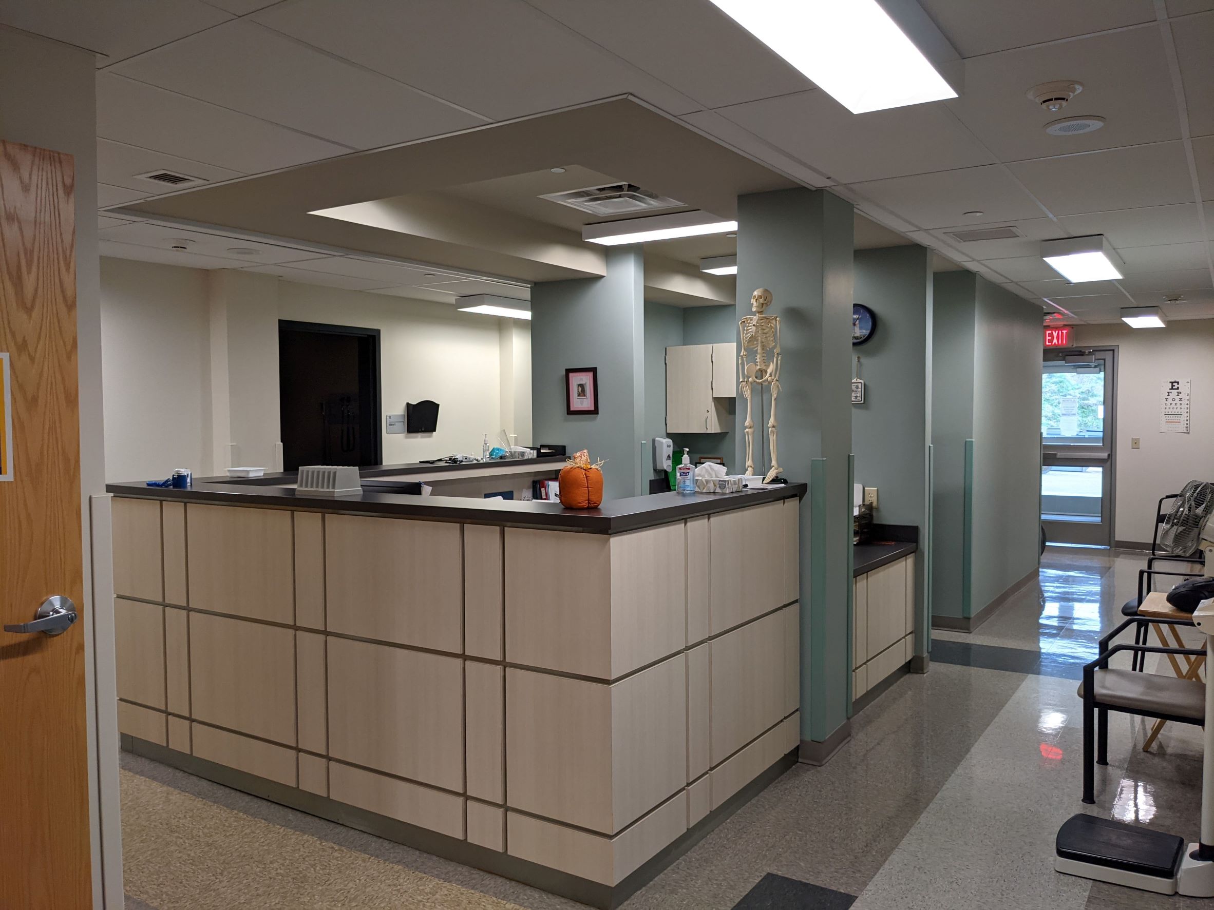 Nurses offices with vinyl floor tiles, sage green walls and columns, natural wood contemporary grided desk and ceiling tiles with tan bulkhead