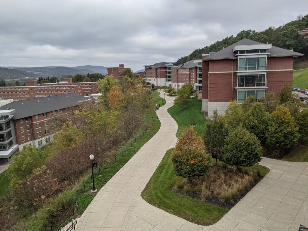 Multiple red brick living learning community residence halls with large glass towers on the ends, straddling a long winding sidewalk on the side of a mountain in Pennsylvania
