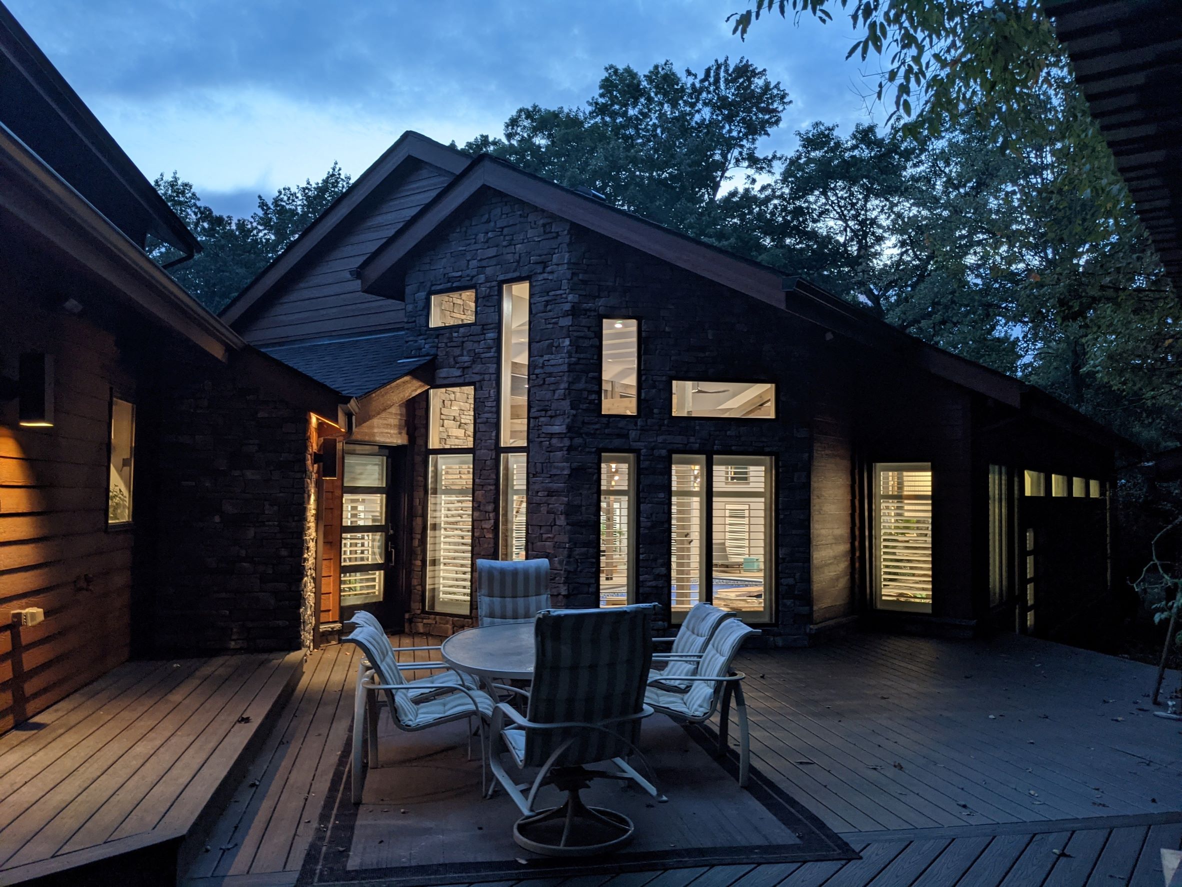 Stunning dusk view of deck area in foreground with Contemporary House addition with stone, wood siding and modern geometric window design with light spilling out of windows outside of Pittsburgh Pennsylvania