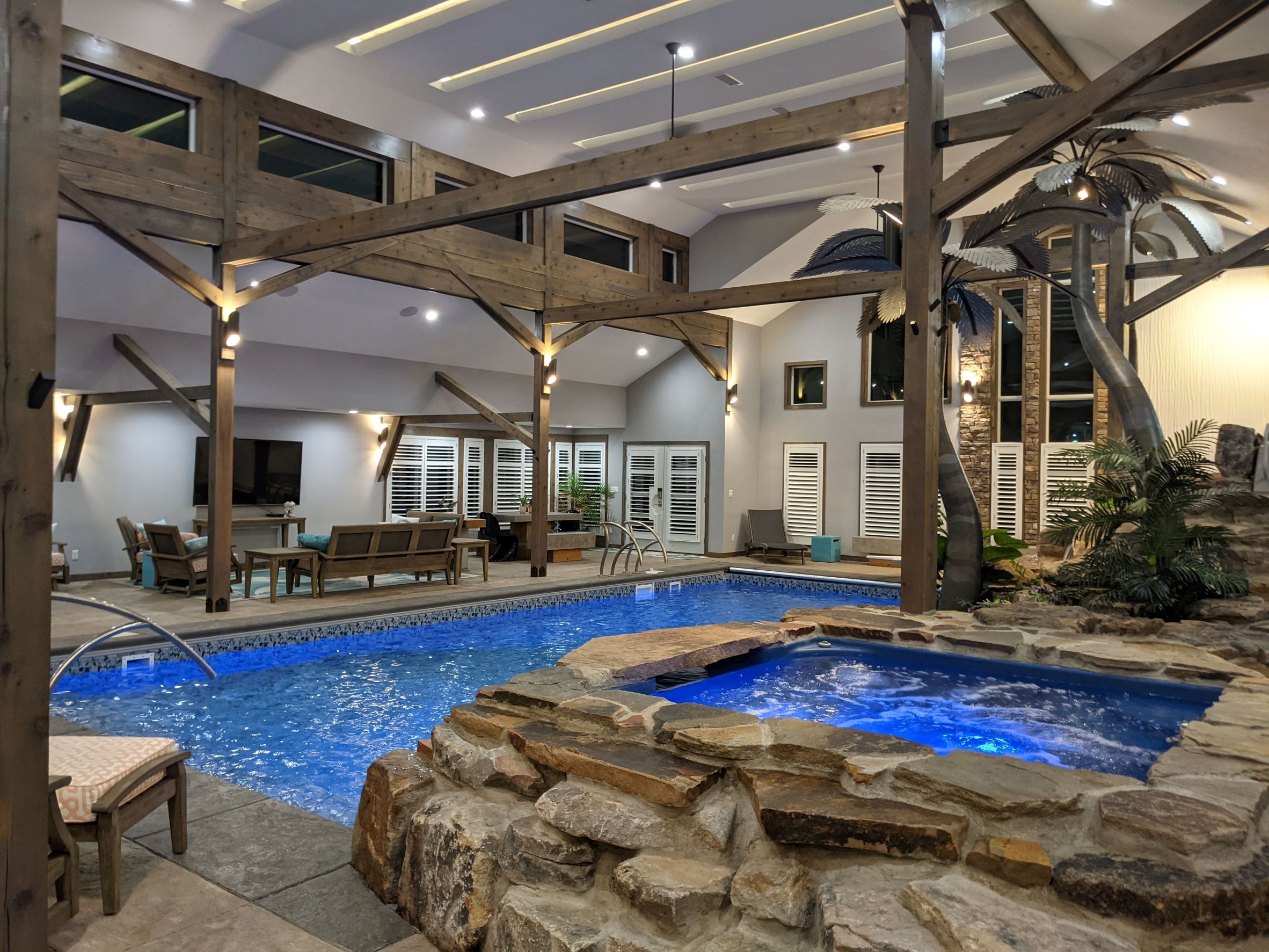 Interior View of Residential Pool Addition to Private Home with hot tub in foreground with stone with swimming pool and waterfall in background and palm trees, wood timber beams and columns outside of Pittsburgh Pennsylvania