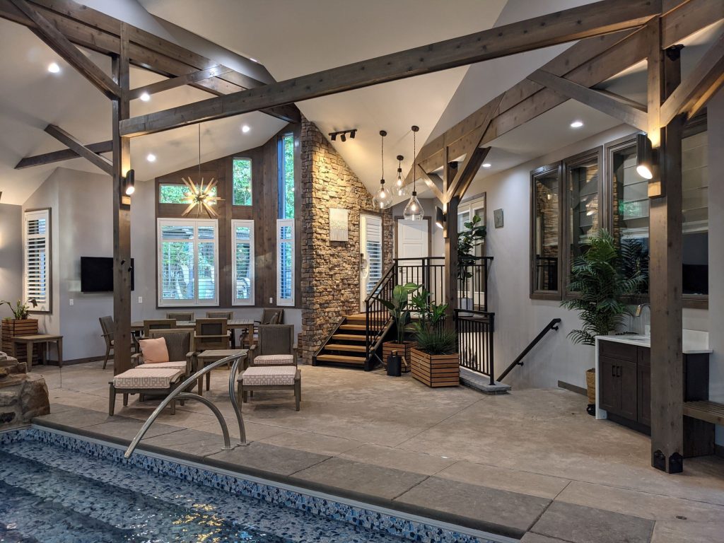 Interior View of Residential Pool Addition to Private affordable Home with Swimming Pool in foreground and decorative stone, geometric windows, and stair in background, modern, creative, dynamic, wow, amazing, beautiful, indoor pool, indoor pool house, creative, affordable addition, renovation