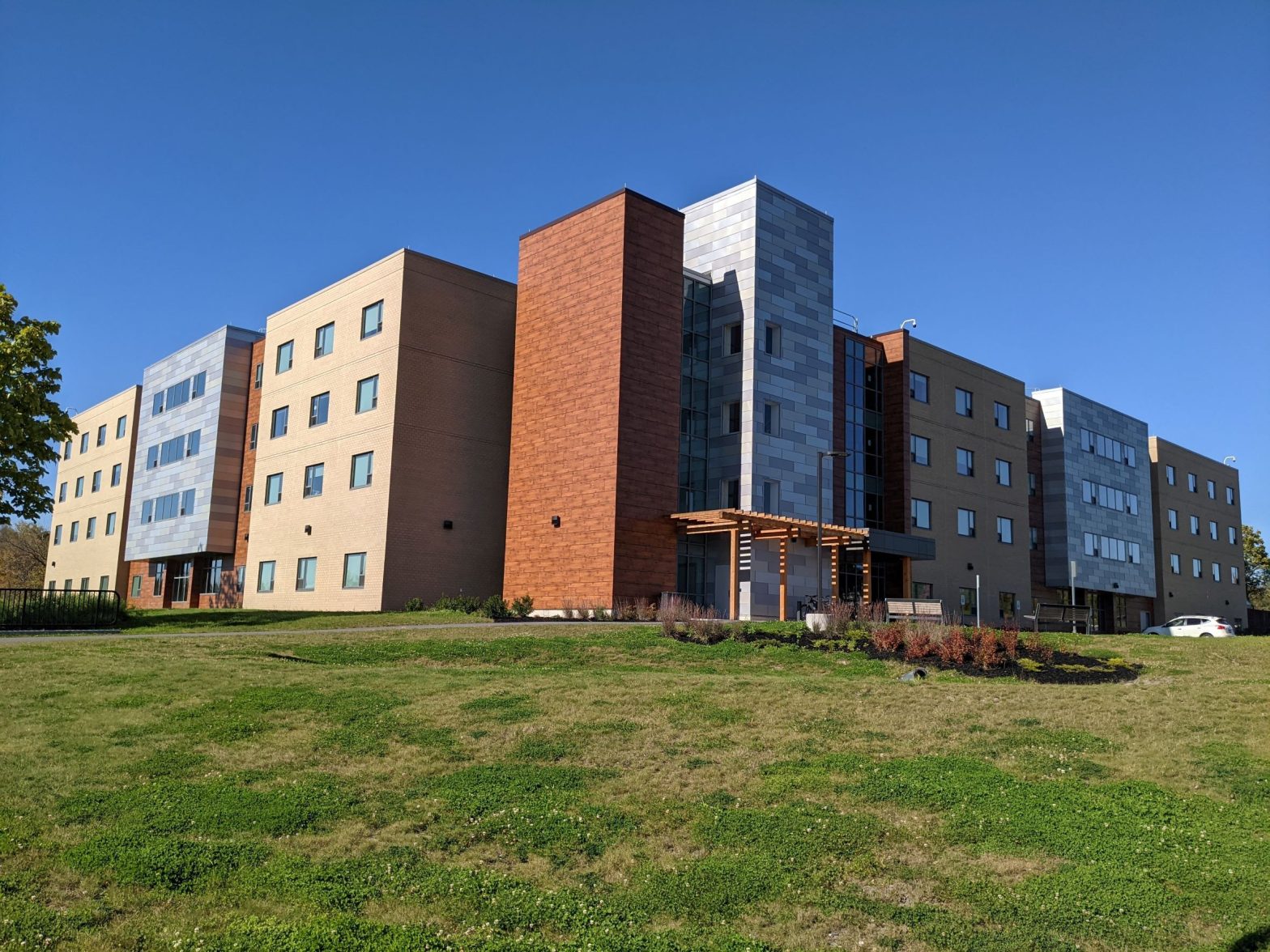 Exterior Overall view of contemporary net-zero energy, zero-net carbon dormitory with brick, metal panel and wood with a large wood trellis at the main entry into residence hall.