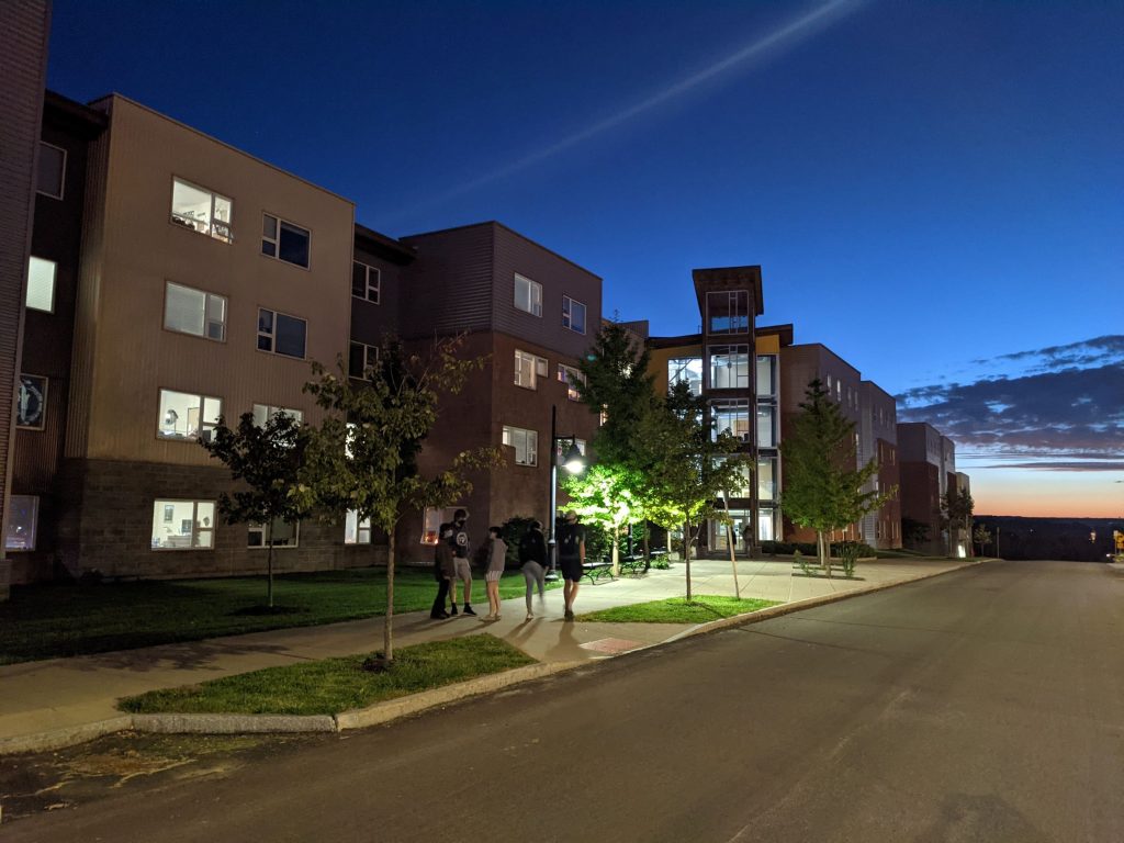 Long discontinues building with large wooden ranger tower lit up at night with sunset in background, appears as a row of many rowhouses in New York 