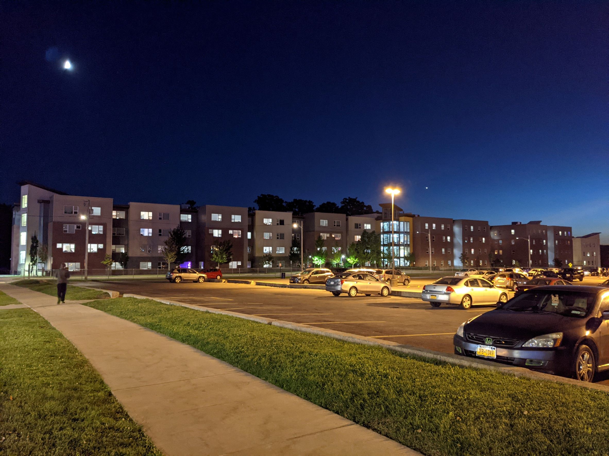 Night shot of overall Long discontinues student housing building with large wooden ranger tower lit up at night with sunset in background, appears as a row of many rowhouses