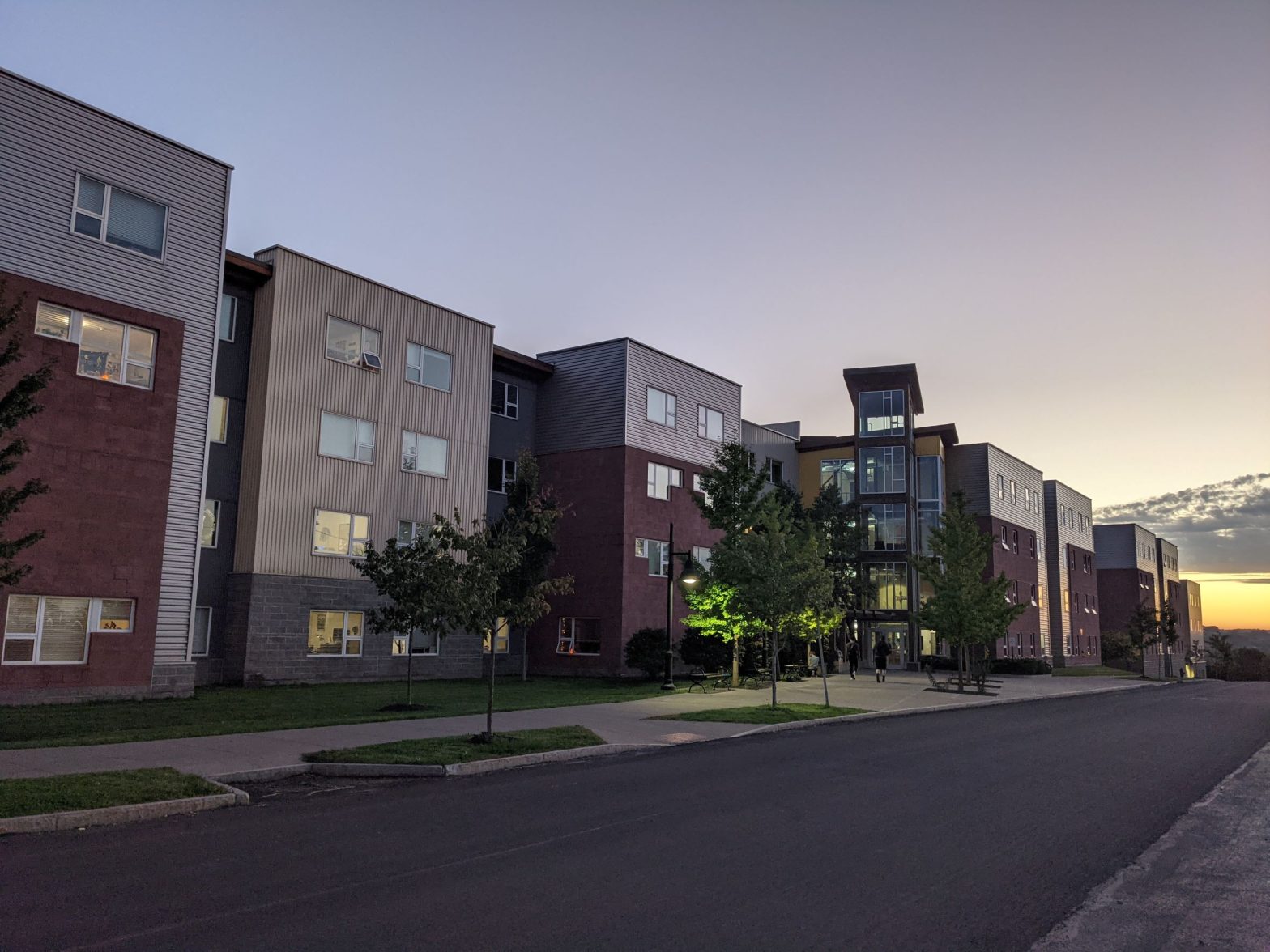 Long discontinues student housing building with large wooden ranger tower lit up at night with sunset in background, appears as a row of many rowhouses